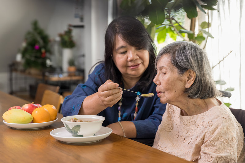 Een Aziatische vrouw helpt haar bejaarde moeder met eten